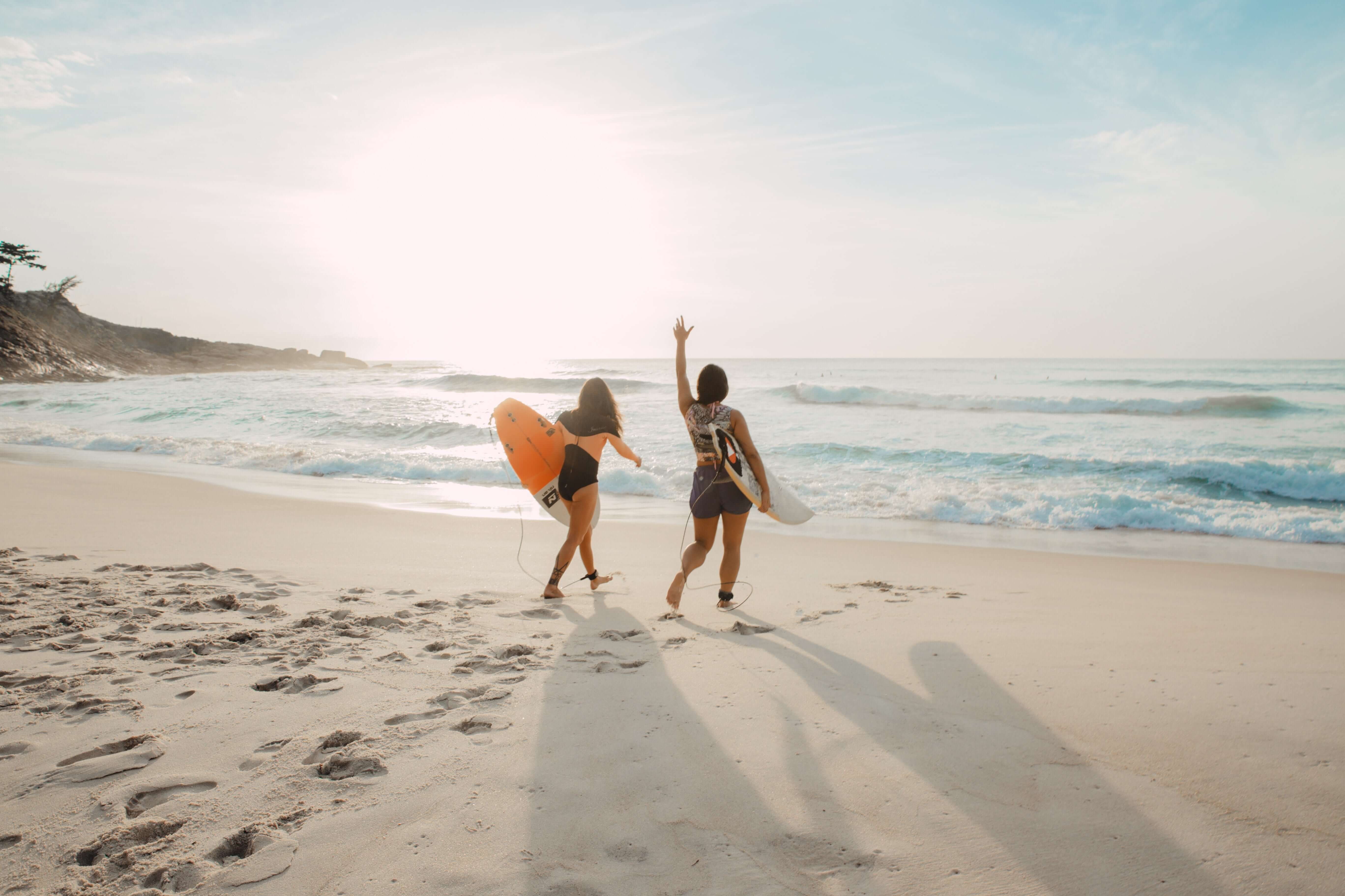 two women going surfing on beach at sunset